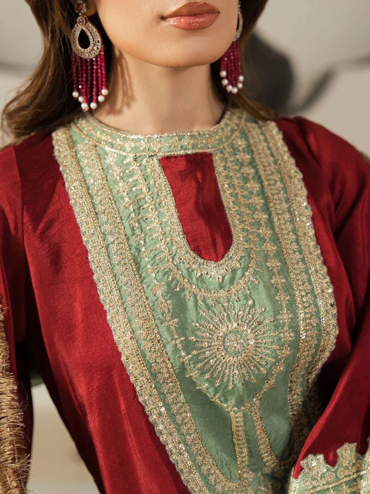 Elegant maroon ethnic outfit with traditional gold threadwork and a contrasting mint green shawl.