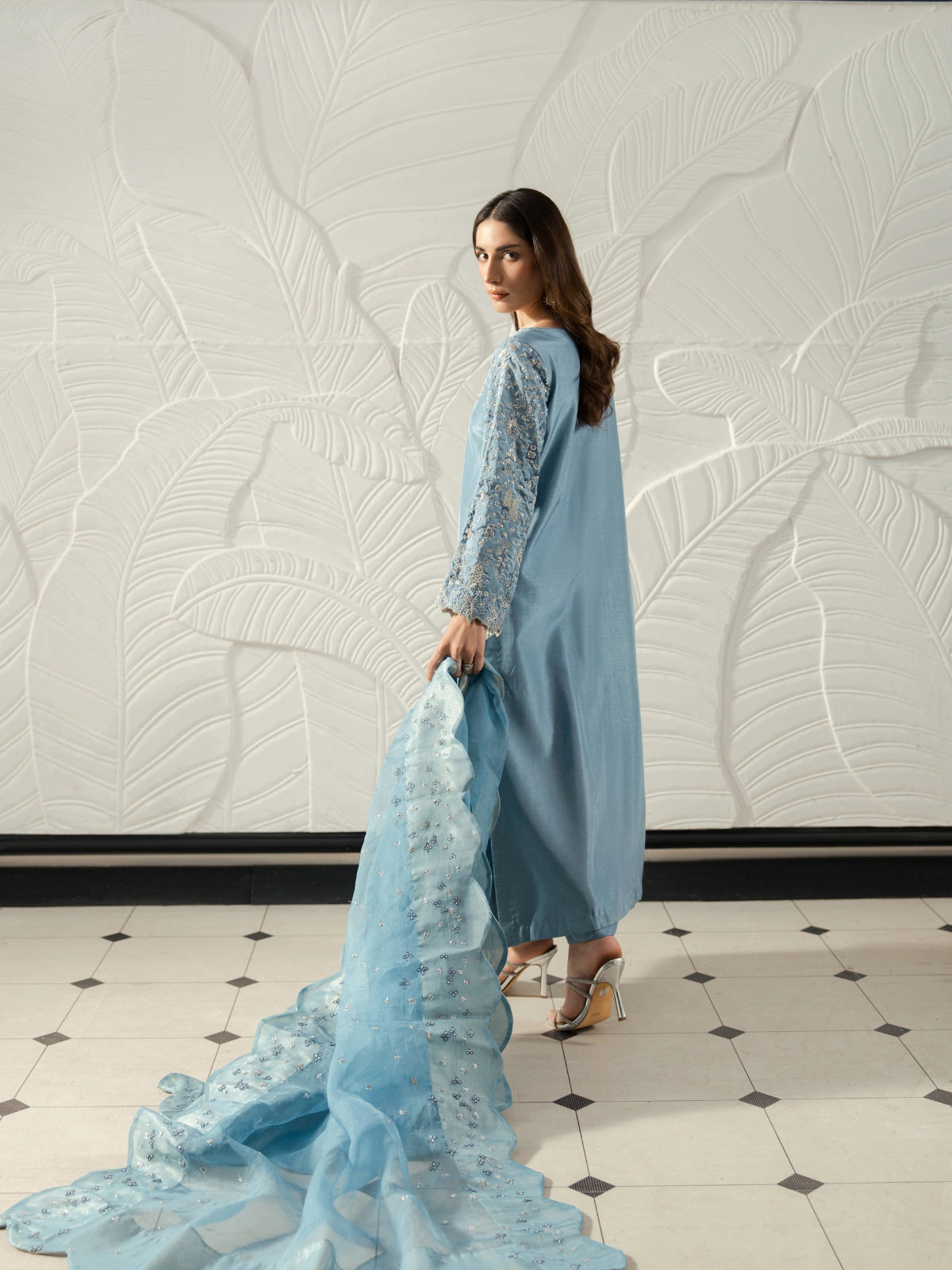 Model wearing a sky blue Pakistani suit with a scalloped embroidered dupatta and silver accents.