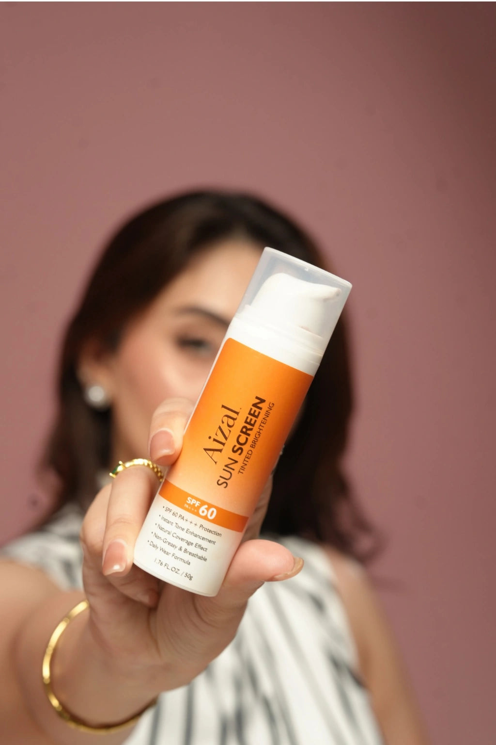 A woman holding Aizal. Sun Screen SPF 60 tinted brightening sunscreen